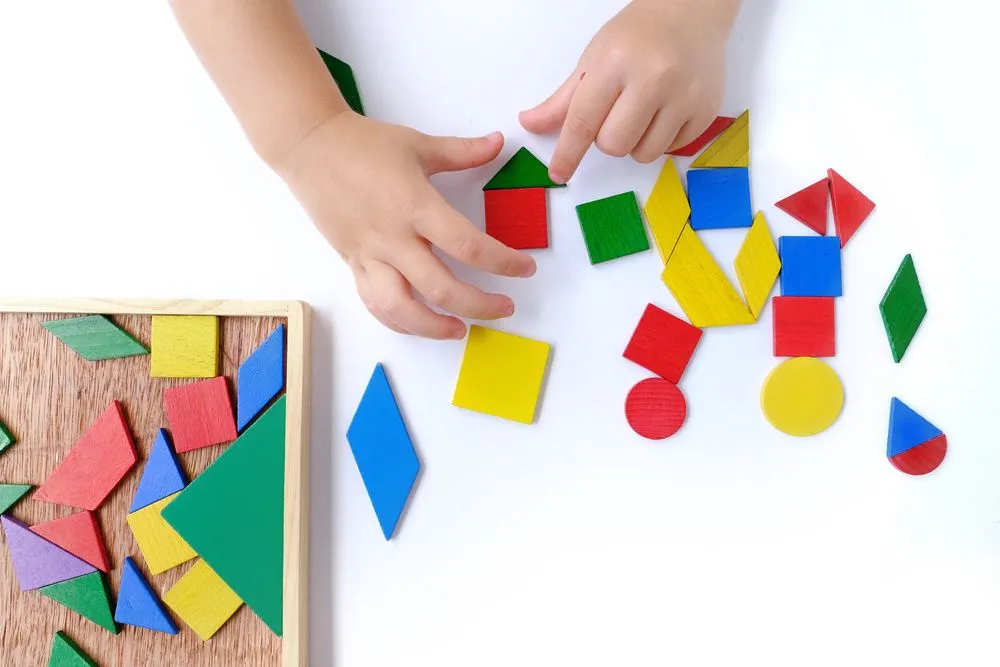 Children's hands create pictures from colored wooden geometric shapes