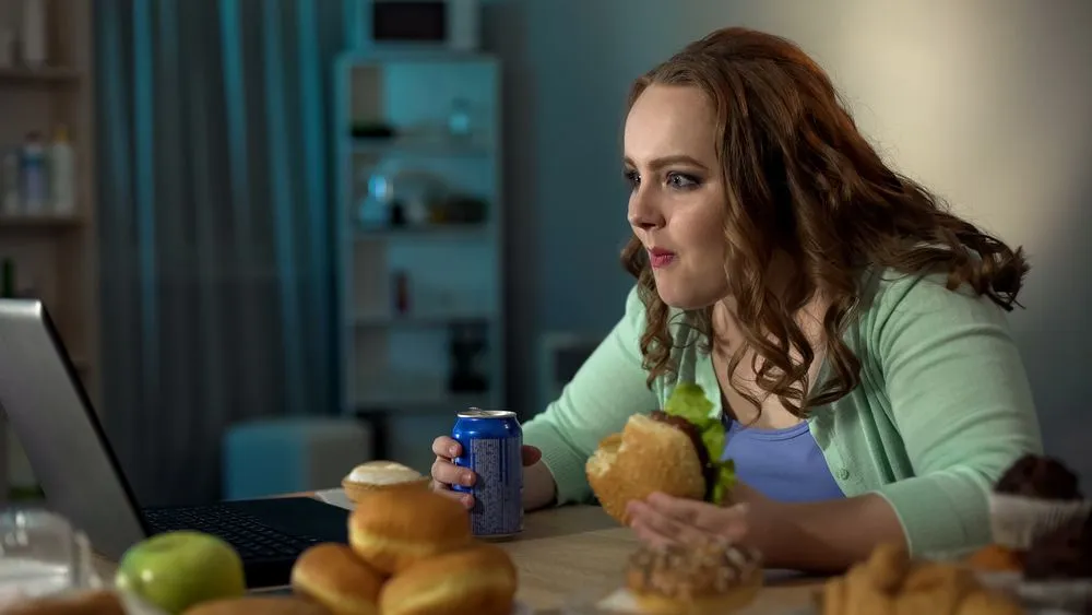 A woman enjoys a bread sandwich while watching a video on her laptop.